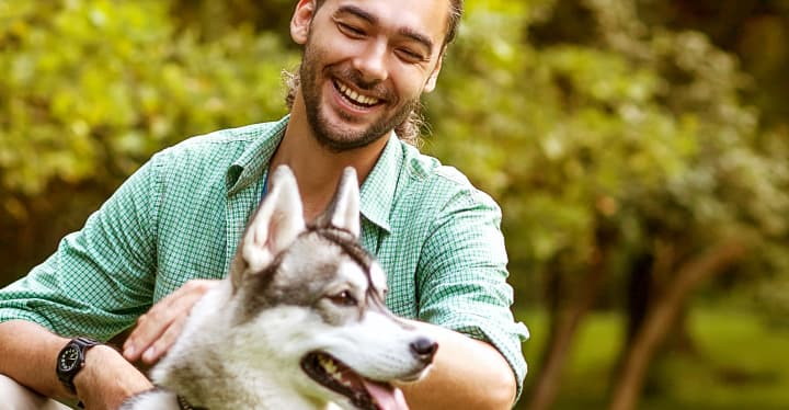 smiling man crouched down, petting a dog