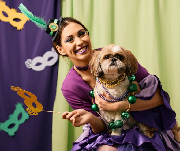 Dog and owner Halloween costumes featuring a woman and her Shih Tzu in matching Mardi Gras outfits with beads and masks.