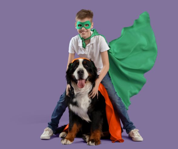 Dog Halloween costumes boy featuring a child dressed as a superhero with his large dog in a matching cape.