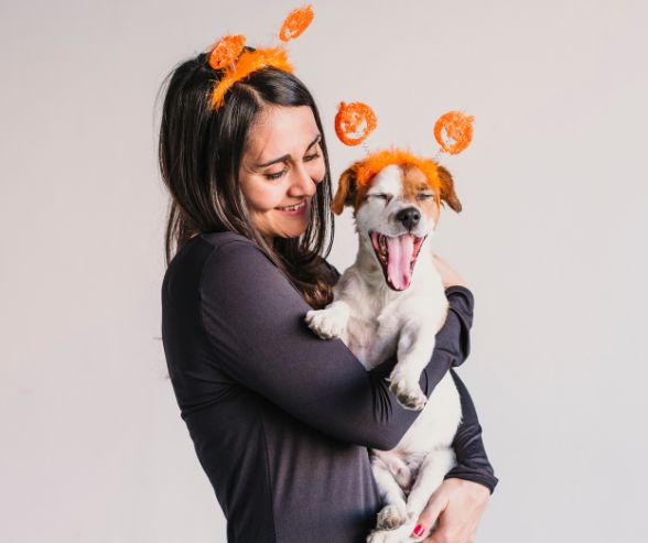Dog and owner Halloween costumes featuring a woman and her dog in matching orange antenna headbands, sharing a cute moment.